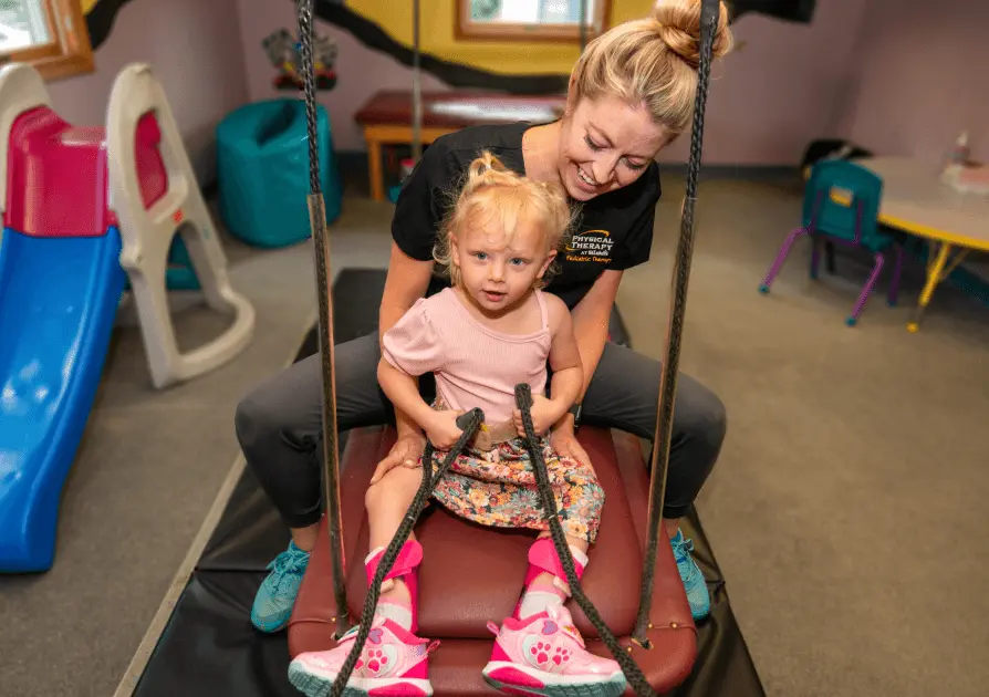 Physical Therapist helping young child swing