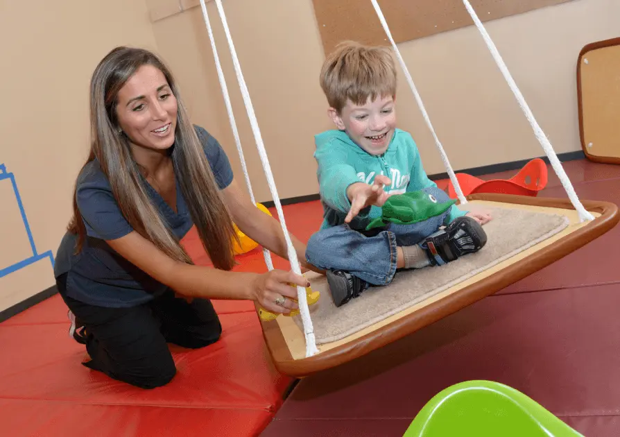 Physical Therapist helping young child on a swing